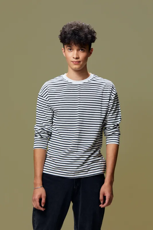 young man with curly hair wearing striped shirt standing relaxed against plain olive background with calm expression and casual posture