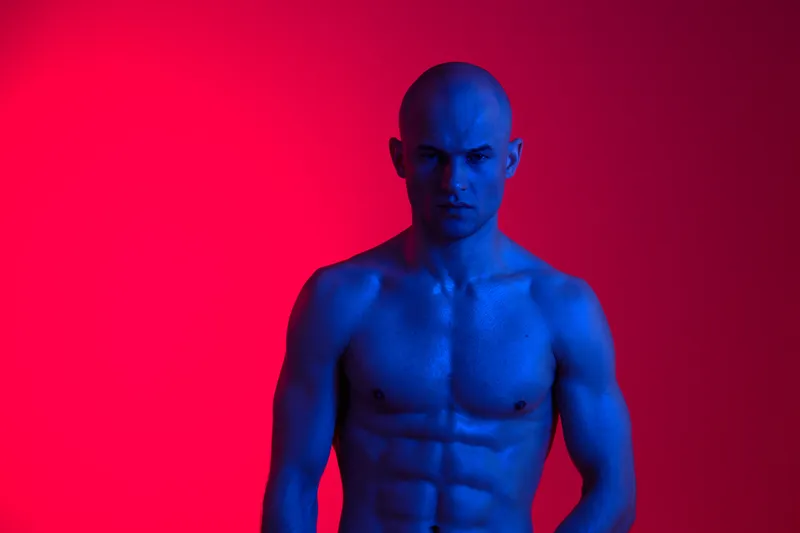 Artistic portrait of a muscular man with blue skin, set against a vibrant red background. This striking, colorful image evokes a sense of strength and confidence.