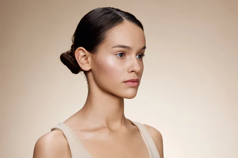Natural beauty portrait of an elegant model with neutral makeup, showcasing a serene expression against a soft beige background, ideal for wellness concepts and beauty promotions