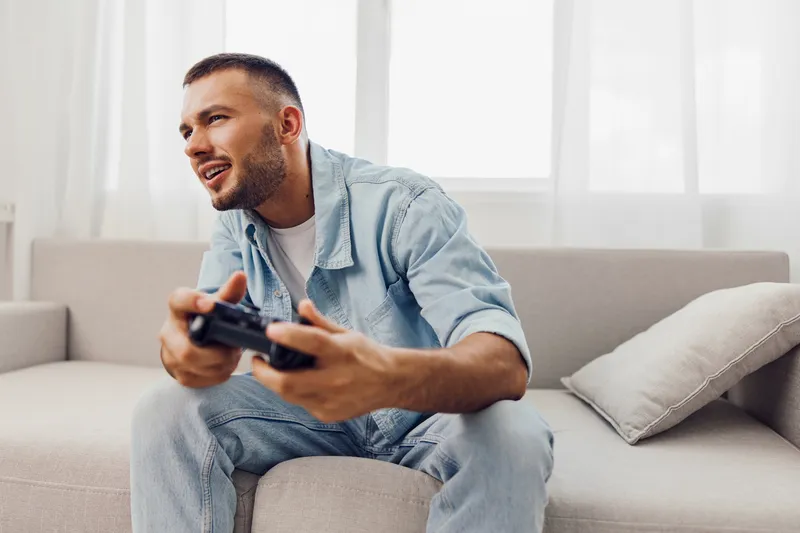 Engaged man enjoying a video game in a bright living room, showcasing excitement with a joyful expression while sitting on a cozy couch.