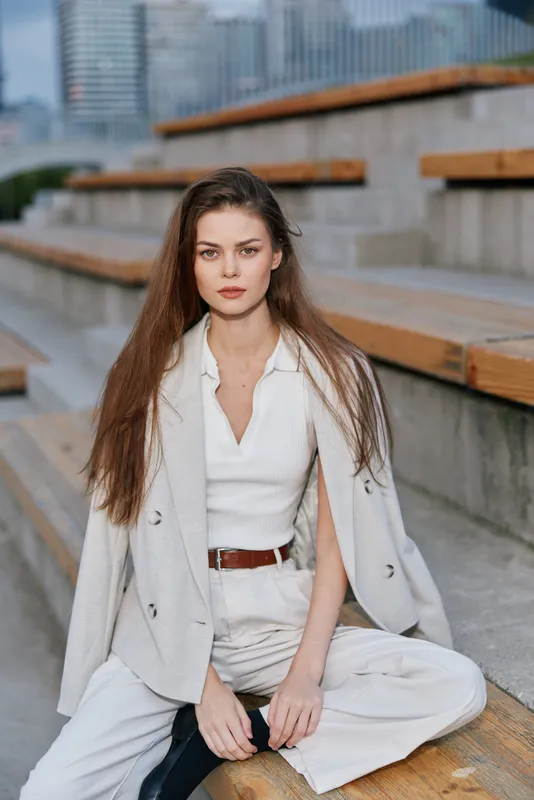 Young woman in beige business casual suit sitting on urban stairs with confident expression, natural light, modern fashion style, autumn season