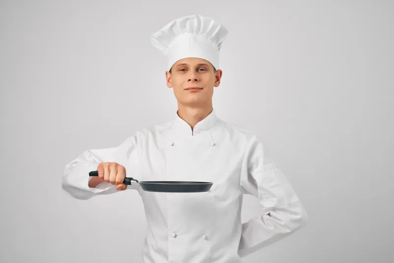 Мужчина в форме повара держит в руке сковороду и готовит еду на кухне