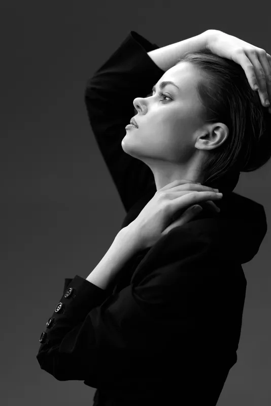 Black and white profile portrait of a thoughtful woman posing with elegant style and confident expression in dark clothing.