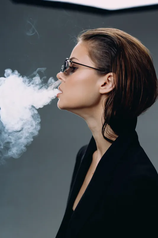 Profile of a young woman wearing glasses exhaling vapor against a dark background in a modern style.
