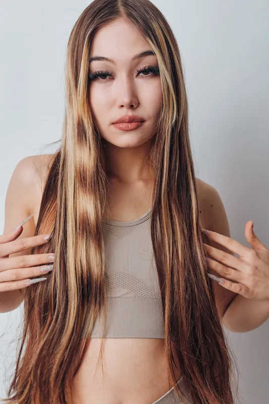 Young woman with long straight hair posing in tank top isolated on light background. Beauty, fashion and hairstyle concept with confident female looking at camera closeup.