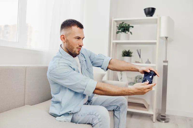 Engaged man enjoying video gaming, showcasing emotion and concentration while playing in a modern, bright living room setting with stylish decor.