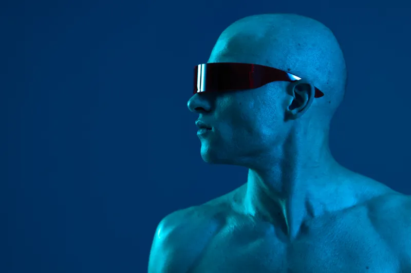 Portrait of a man with futuristic sunglasses, showcasing a striking blue light environment. This captivating image highlights modern aesthetics and innovation.