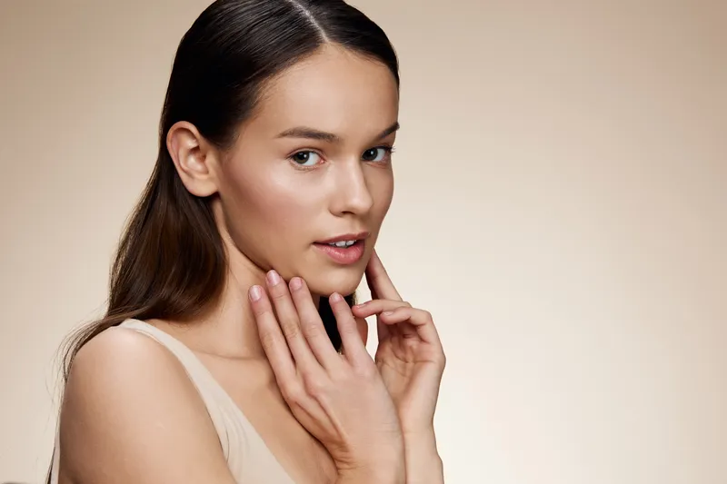 Young woman with natural beauty showcasing skincare routine, soft expression, and minimalistic style on a warm beige background Emphasizing self care and healthy skin