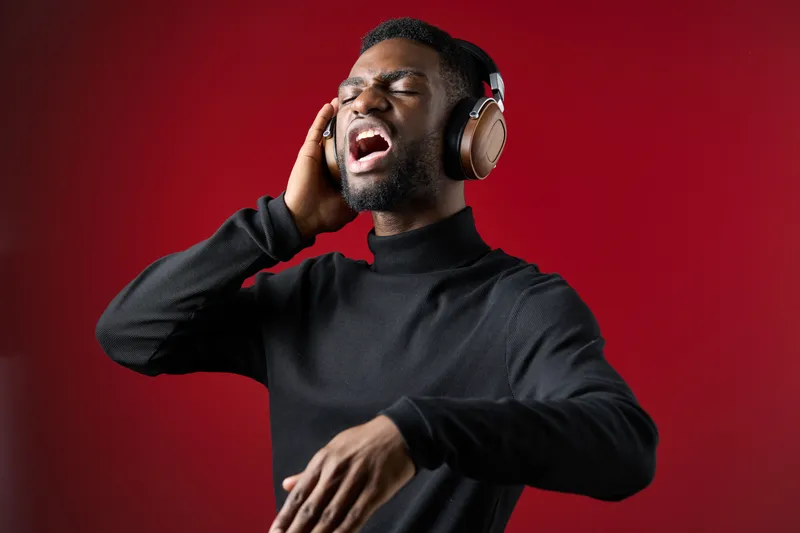 Young Black man passionately singing with headphones on a vibrant red background, expressing joy and creativity through music