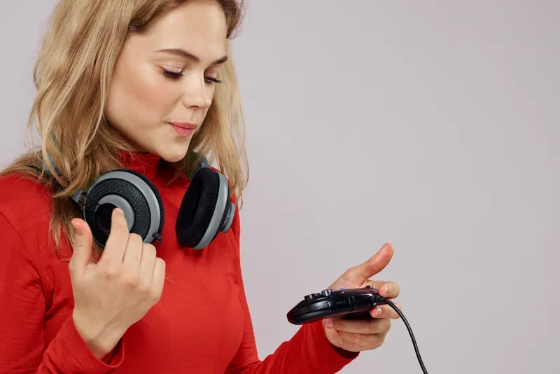 Женщина с наушниками, контроллер в руках, игровая консоль, игра, весёлый досуг, красная куртка, образ жизни, светлый фон