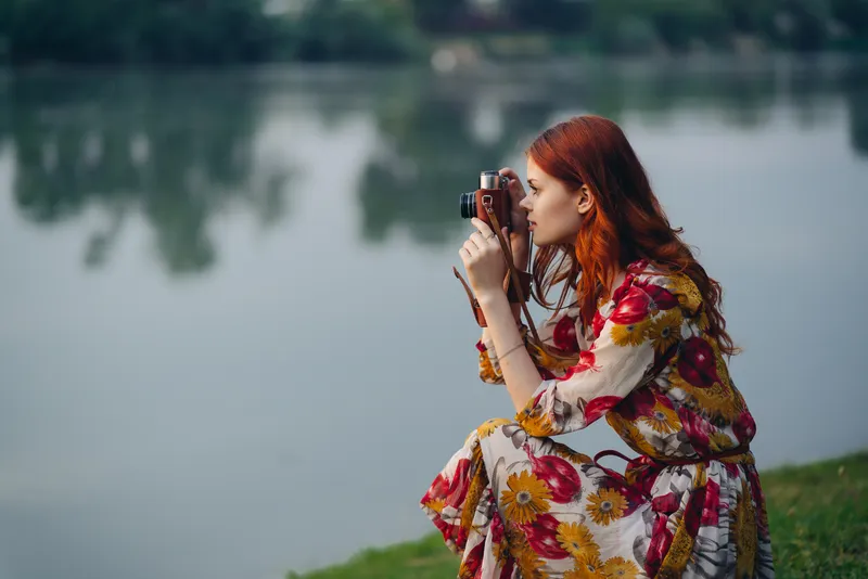 Симпатичная женщина с фотоаппаратом стоит у озера, отдыхая на природе