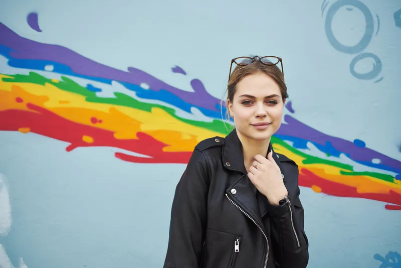 На улице возле красочной стены в городе идёт симпатичная женщина