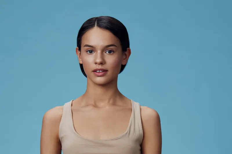 Portrait of a young woman with a natural look against a light blue background showcasing a minimalist style and healthy beauty concept, ideal for wellness and lifestyle content