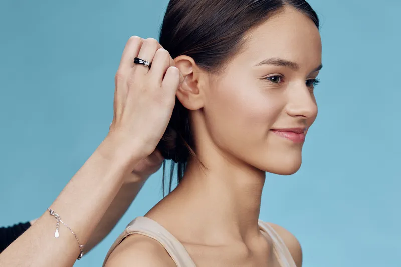 Young woman with natural makeup smiling as stylist adjusts her hair against a soft blue background, embodying beauty and confidence