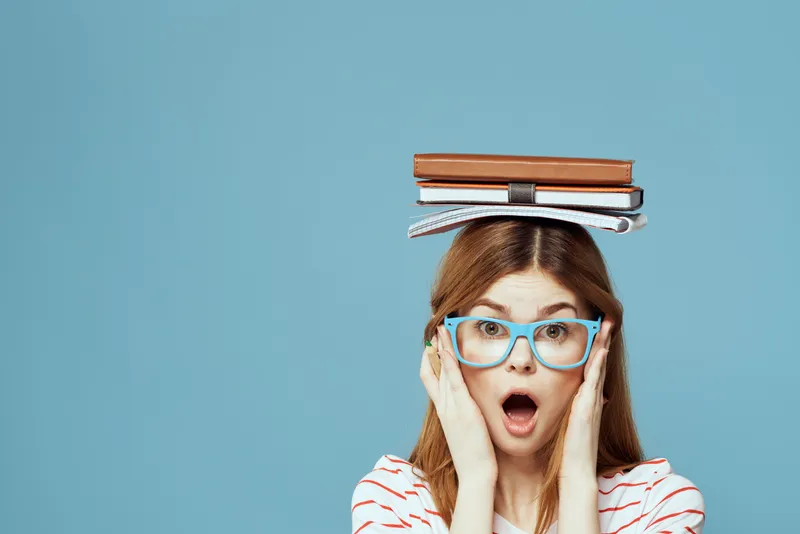 Студентка держит книги на голове на фоне синего цвета, что символизирует научное образование