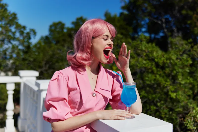 Жизнерадостная женщина с розовыми волосами наслаждается летним освежающим коктейлем