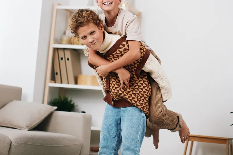 Authentic playful moment featuring a child giving a piggyback ride to a friend at home, capturing warmth, joy, and a casual school life vibe in a cozy living space.
