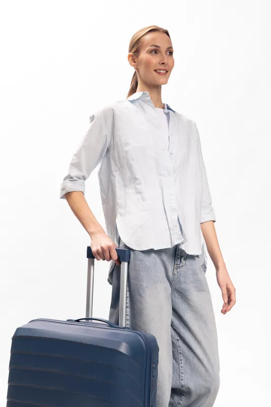 Young woman in casual clothes stands with a suitcase on white background. Travel concept with luggage, trip preparation, and vacation planning. Positive female traveler ready for journey.