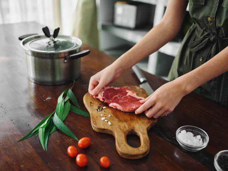 Женщина на кухне готовит ужин из мяса, овощей и специй на деревянном столе на фоне стильной кухни, свежие экопродукты, здоровое питание, образ жизни
