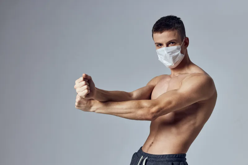 Спортивный мужчина с мускулистым телом в медицинской маске позирует в спортзале