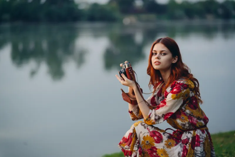 Женщина с фотоаппаратом на природе у реки во время отпуска или путешествия