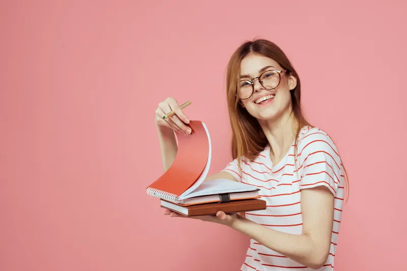 Молодая студентка с книгами на розовом фоне, в очках, крупный план лица