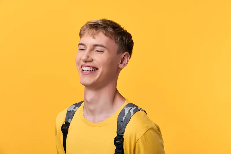 Smiling, happy, cheerful, yellow, casual, fashion, suspenders, male, upbeat, lighting, bright studio image of a young man in a yellow tee and suspenders, conveying positivity, energy and approachable