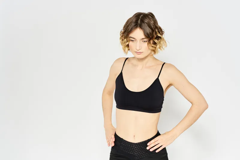 Стройная женщина в леггинсах на светлом фоне выполняет упражнения фитнес-гимнастики