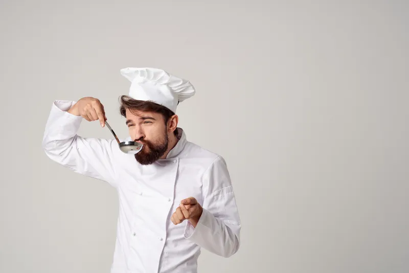 Мужчина в поварской форме пробует еду, профессиональная работа на кухне