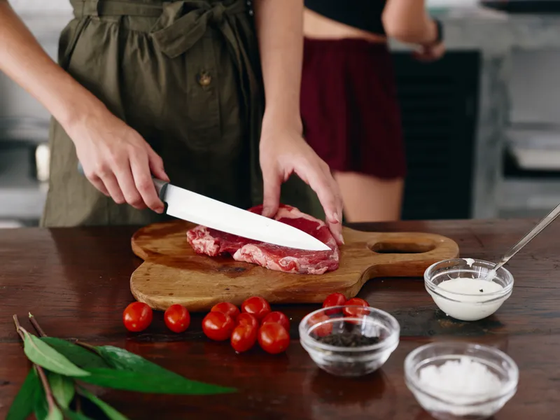 Женщина с ножом в руке нарезает стейк из мяса для жарки на кухне