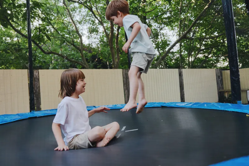 Joyful children playing on a trampoline, showcasing laughter and fun in a vibrant outdoor setting with greenery and sunlight. Perfect for family moments.