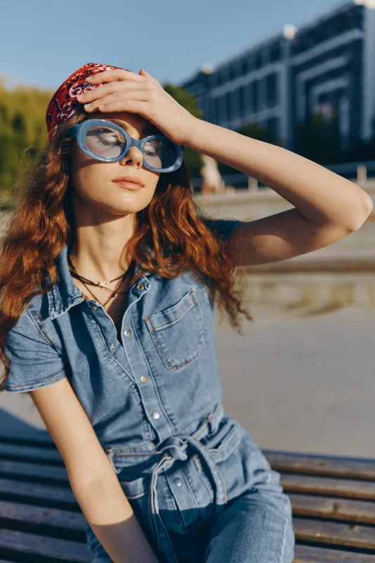 Lifestyle woman in modern boho-western denim street style wearing large sunglasses and a bandana, captured with warm film color tones under natural sunlight.