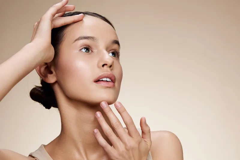 Elegant young woman with natural makeup touching her face, showcasing healthy skin and a calm expression, perfect for beauty and skincare themes