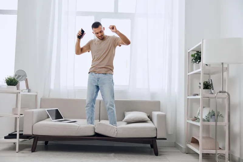 Happy man dancing with smartphone in a bright, modern living room. The cheerful atmosphere features soft colors and a cozy vibe, perfect for creative inspiration.