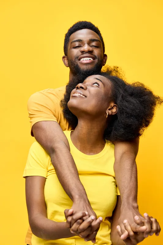 Happy young African couple embracing against a vibrant yellow background, showcasing love and joy in matching outfits, ideal for romantic and lifestyle themes