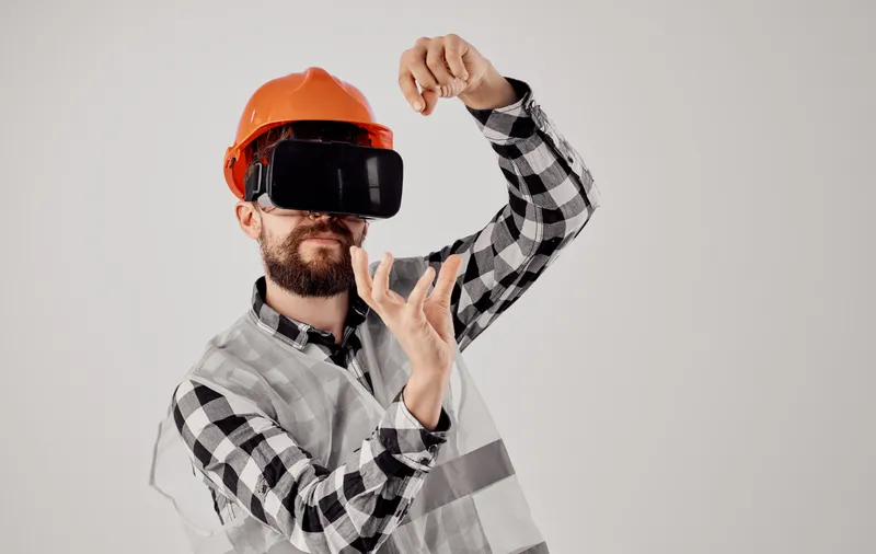 Строитель в оранжевой каске и 3D-очках жестикулирует руками, есть свободное место для текста, светлый фон