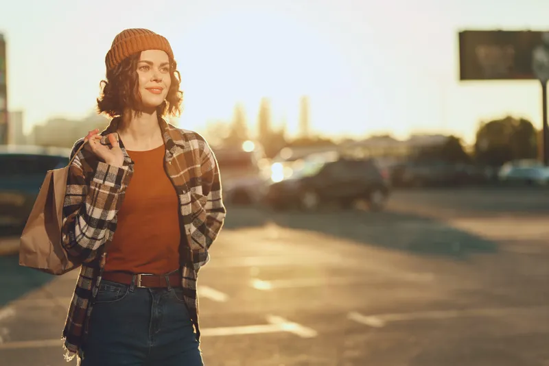 Woman walking in urban street at golden hour glow with shopping bag, candid lifestyle portrait showing authenticity, mindful living and emotional storytelling in warm sunset light.