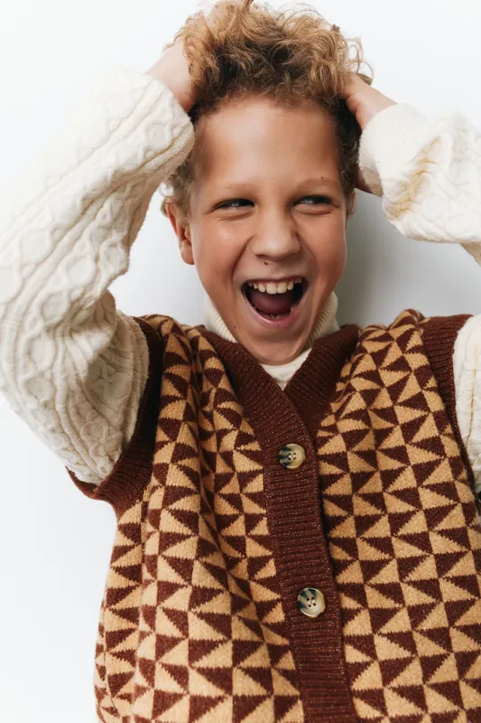Authentic candid moment of a child at school, capturing playful energy, genuine expression, and everyday joy in a cozy knitwear outfit.
