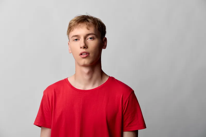 Youth, man, red shirt, casual studio expression with minimal neutral background and clean lighting for fashion oriented stock image highlighting confidence and modern style in a simple indoor setting