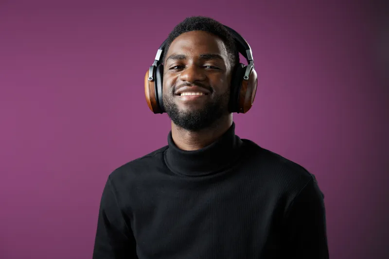 Smiling young African man in headphones enjoying music with a purple background, showcasing joyful emotions and a modern style