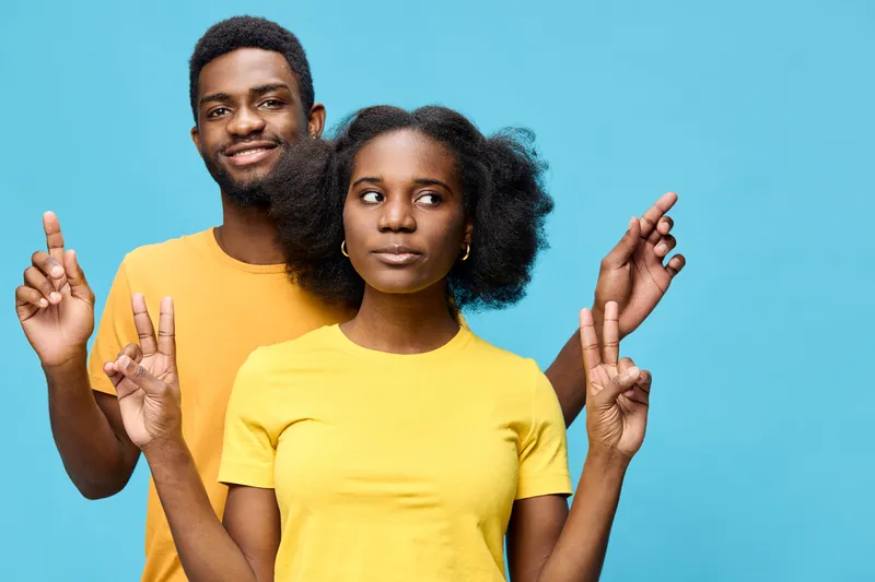 Happy young African American couple playfully posing with peace signs against a bright blue background, wearing matching yellow t shirts, conveying joy and connection