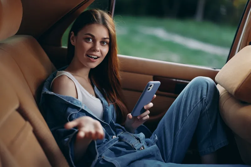 Young woman sitting in a car with a smartphone, expressing surprise, casual style, denim outfit, vibrant green background, perfect for social media themes.