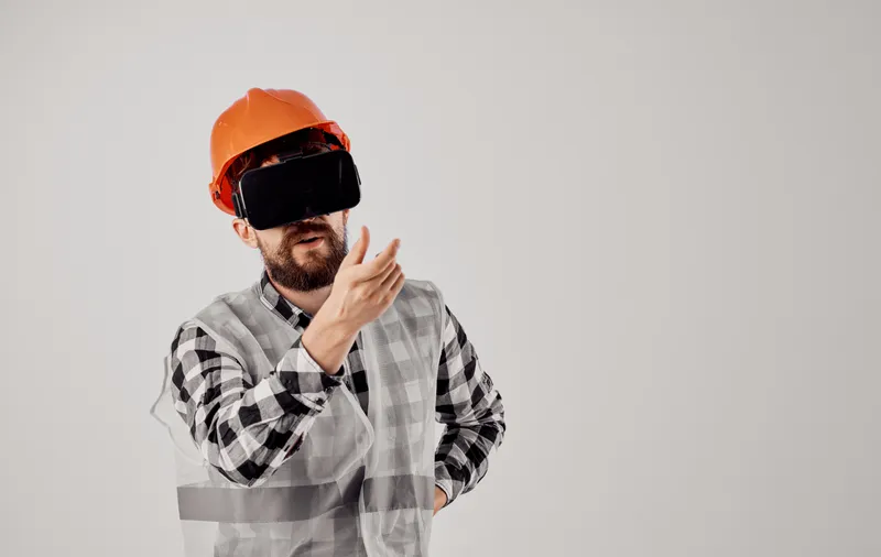 Инженер-строитель в оранжевой каске, клетчатой рубашке, 3D-очках, жестикулирует руками