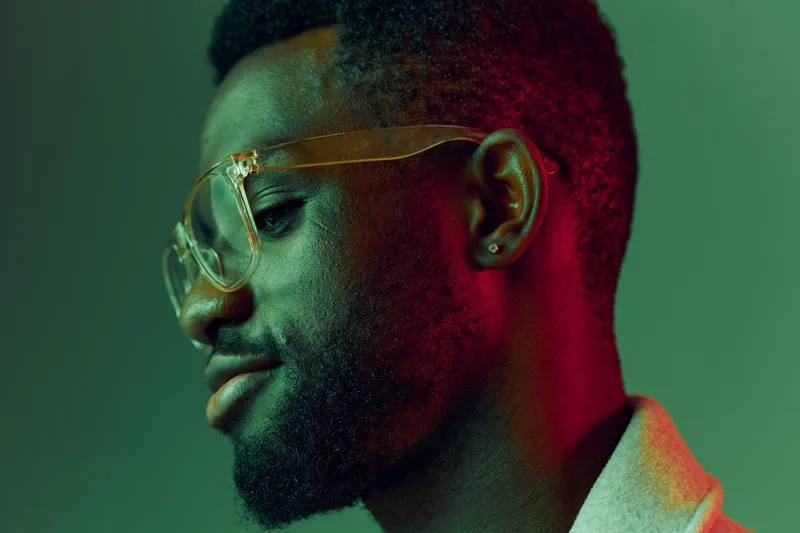 Portrait of a young Black man with stylish glasses, expressing confidence against a colorful gradient background, ideal for modern lifestyle themes