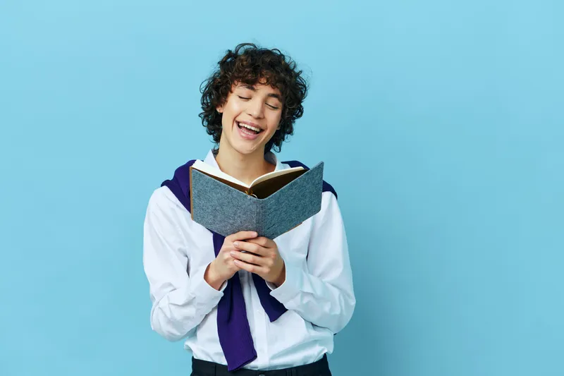 Студент с книгой в колледже, одетый в куртку, на синем фоне