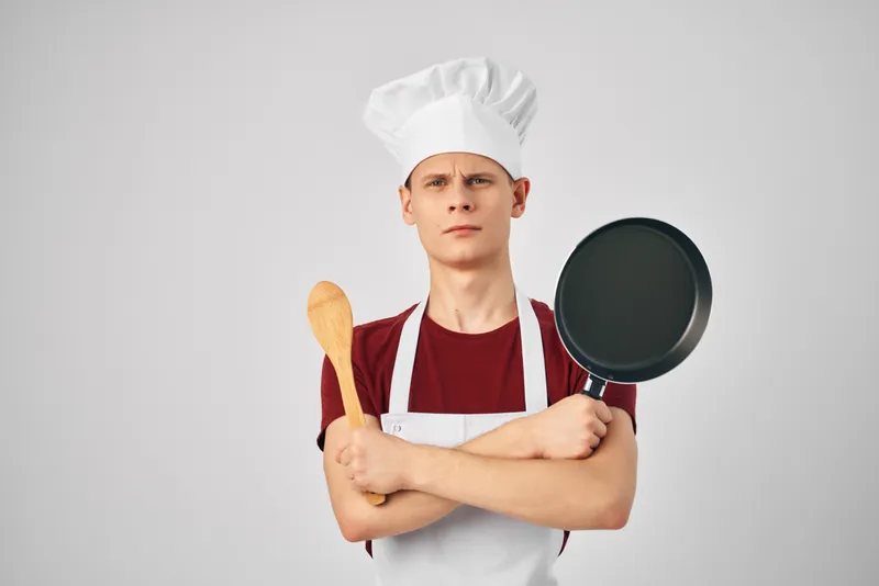 Повар-мужчина держит в руках сковороду на кухне, занимаясь приготовлением пищи