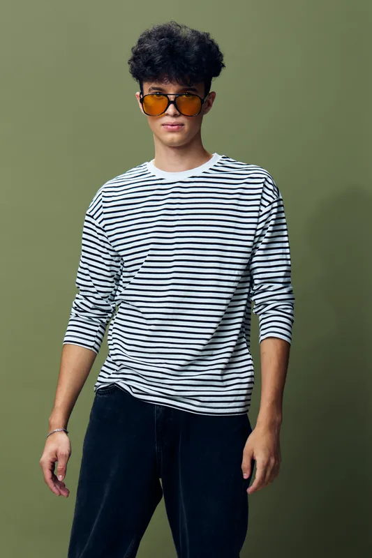 young man wearing sunglasses and striped shirt standing confidently against plain green background with casual style and curly hair, modern fashion portrait