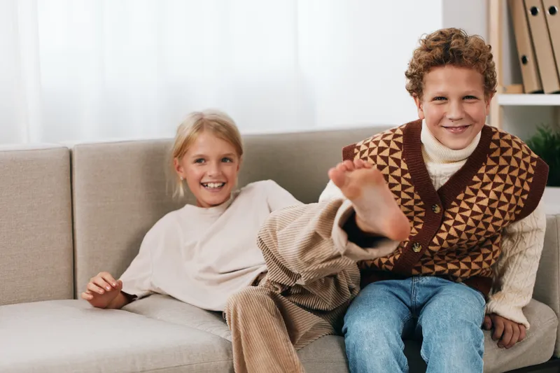 Authentic candid scene showing siblings at home after school, engaged in a playful moment on a cozy sofa with warm light and relaxed everyday lifestyle.