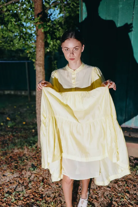 woman dress portrait outdoors night shadow fashion holding vintage serious, model in yellow skirt, authenticity inclusivity moody evening scene