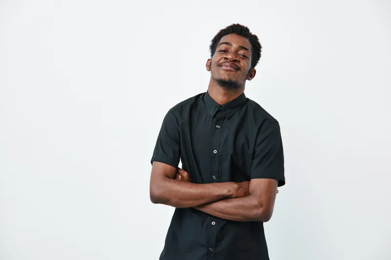 African American man with dark skin wearing black shirt standing with arms crossed smiling confidently on white background. Portrait of young male adult.
